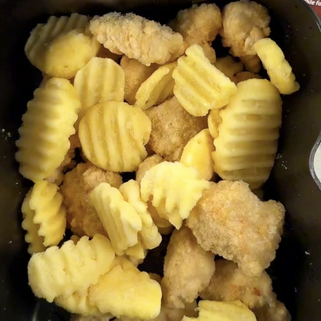 Frozen chicken chunks and crinkle cut chips in an air fryer basket before cooking