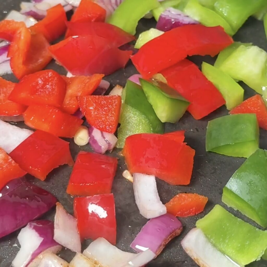 Chopped red pepper, green pepper and red onion frying in a pan