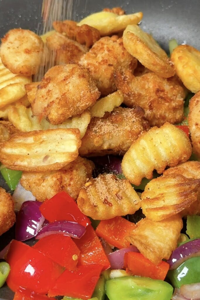 Crispy cooked chicken chunks and chips being added to the pan with peppers and onion