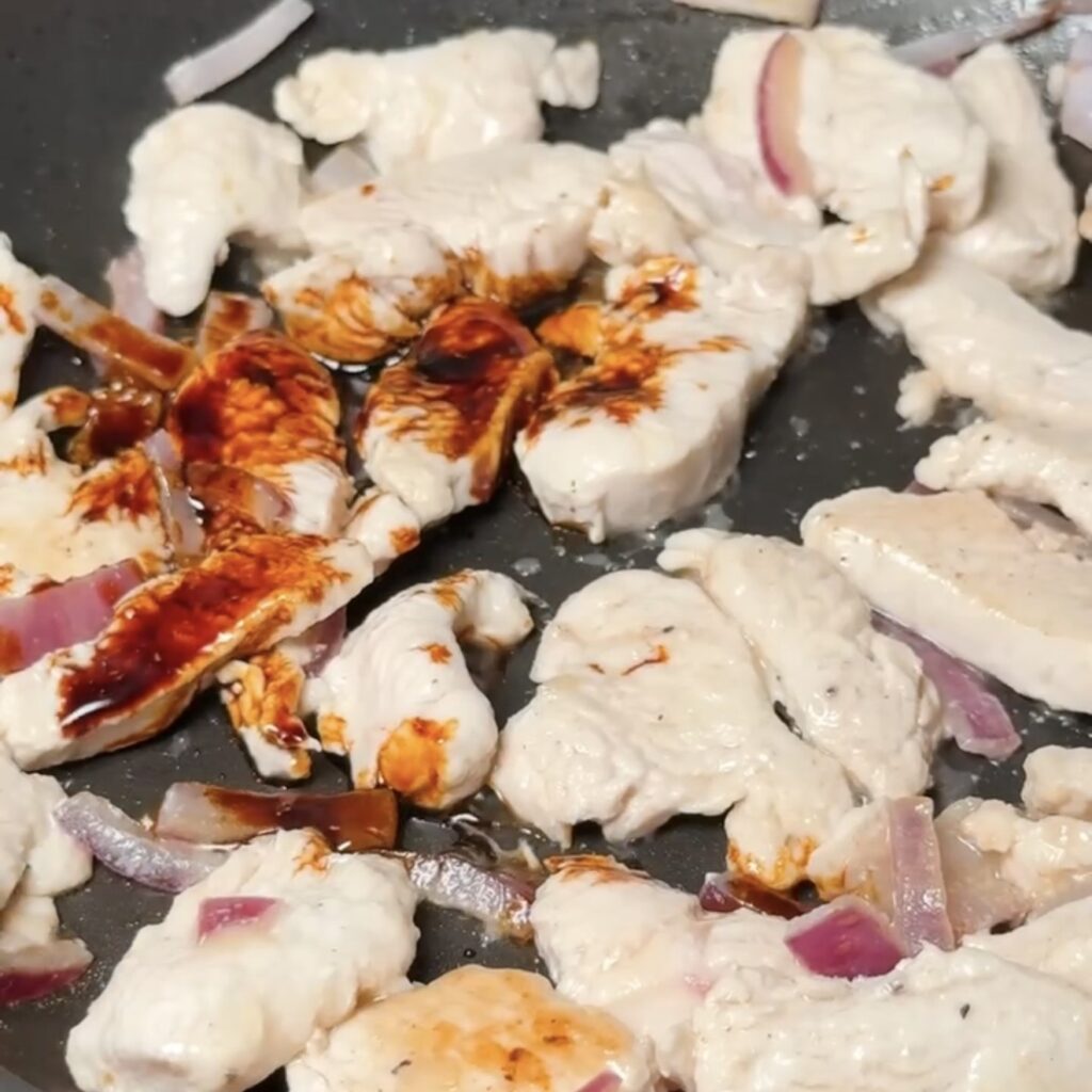 Sliced chicken breast and red onion frying in a pan with light soy sauce