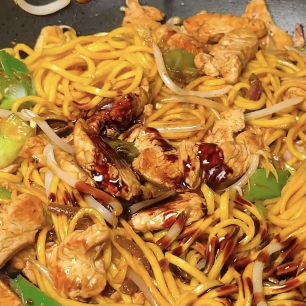 Chicken chow mein with glossy noodles, spring onions and dark soy sauce in a wok