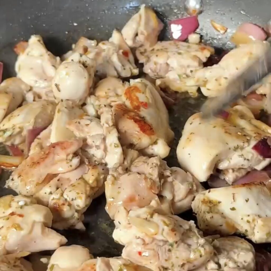 Seasoned chicken thigh pieces frying with onion in a pan