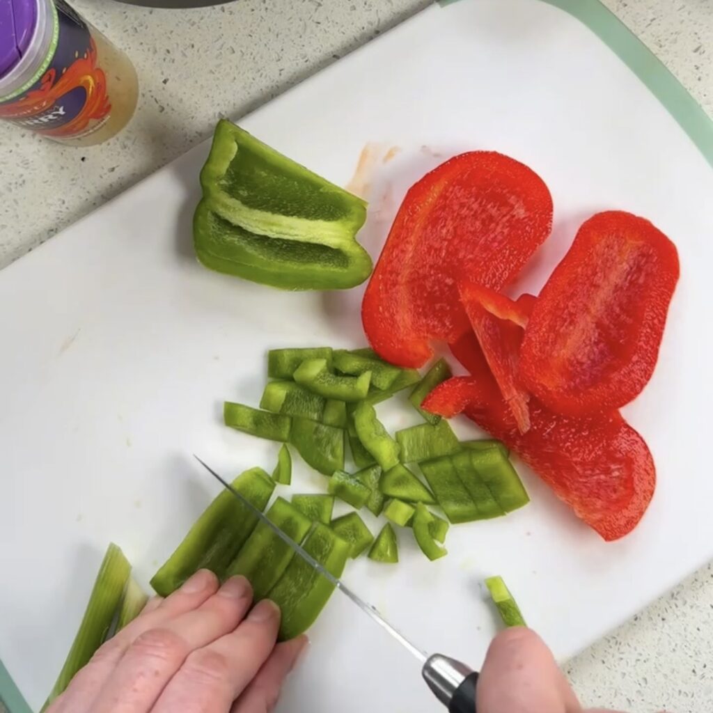 Green and red pepper being chopped on a white chopping board with Schwartz curry powder in the background
