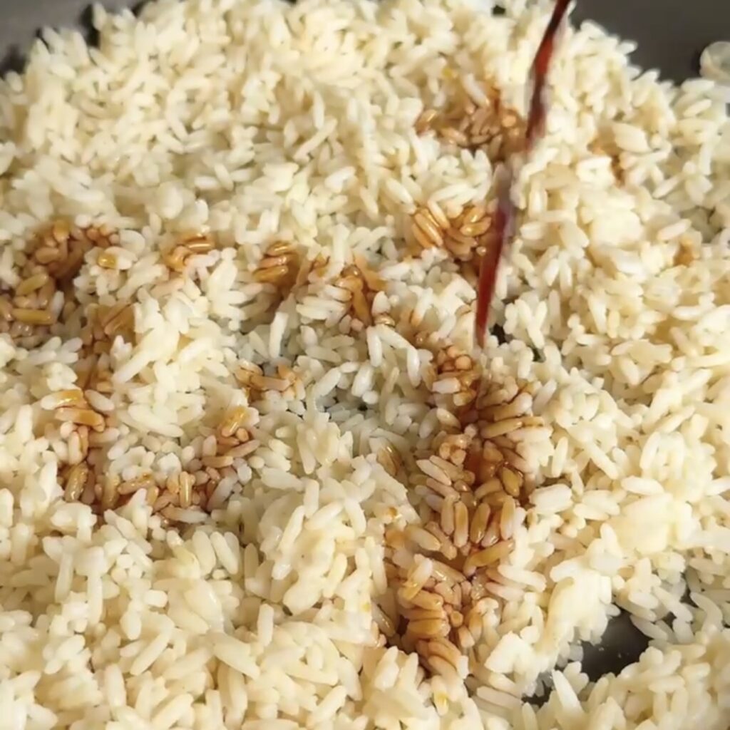 Cold cooked long grain rice being stirred in a hot pan with a wooden spoon