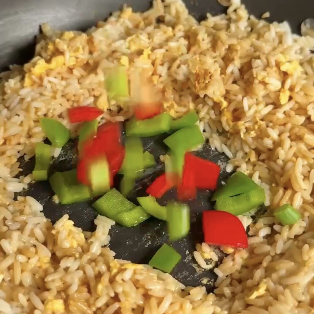 Chopped red and green peppers being added to fried rice in a pan