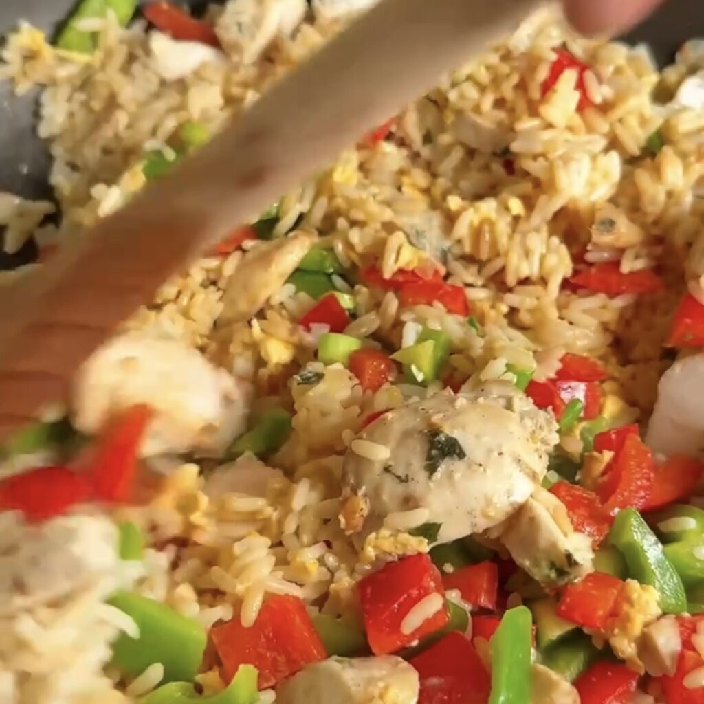 Chicken pieces being stirred into fried rice with peppers in a hot pan