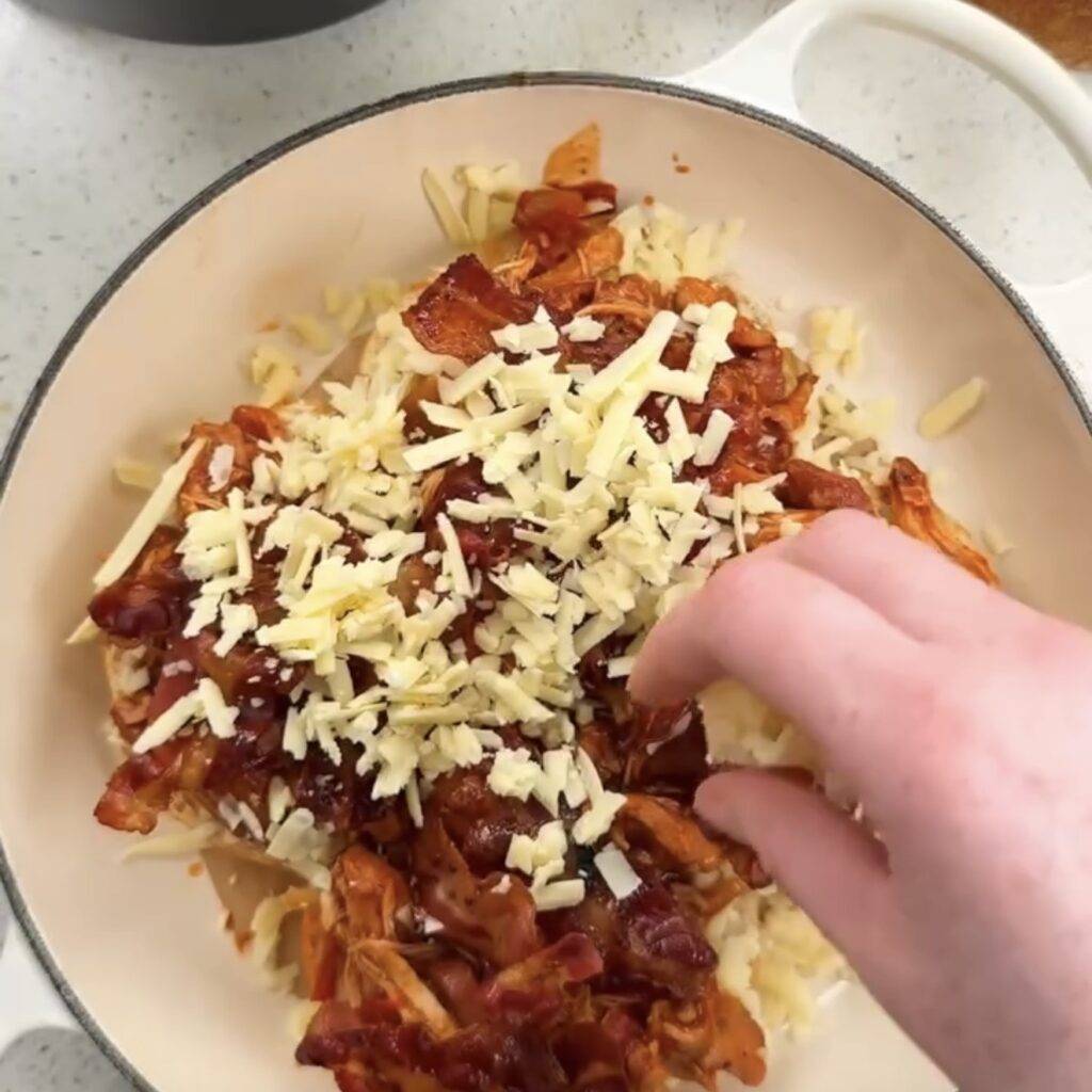 Grated cheese being sprinkled over the assembled hunter's chicken buns before baking