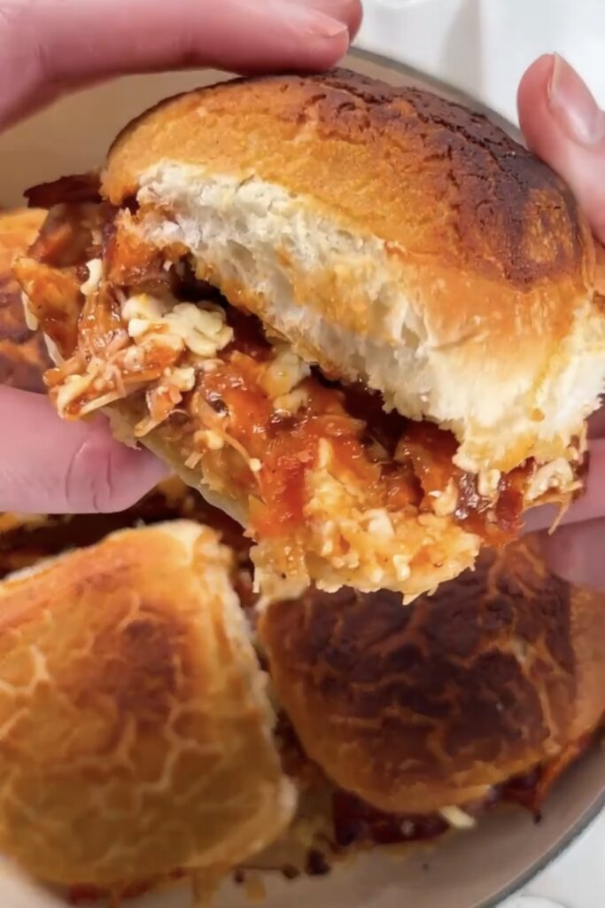 Hands pulling apart a cheesy hunter's chicken bun showing melted cheese, BBQ chicken and crispy bacon