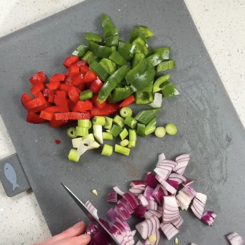 Chopped red pepper, green pepper, spring onion and red onion on a grey chopping board