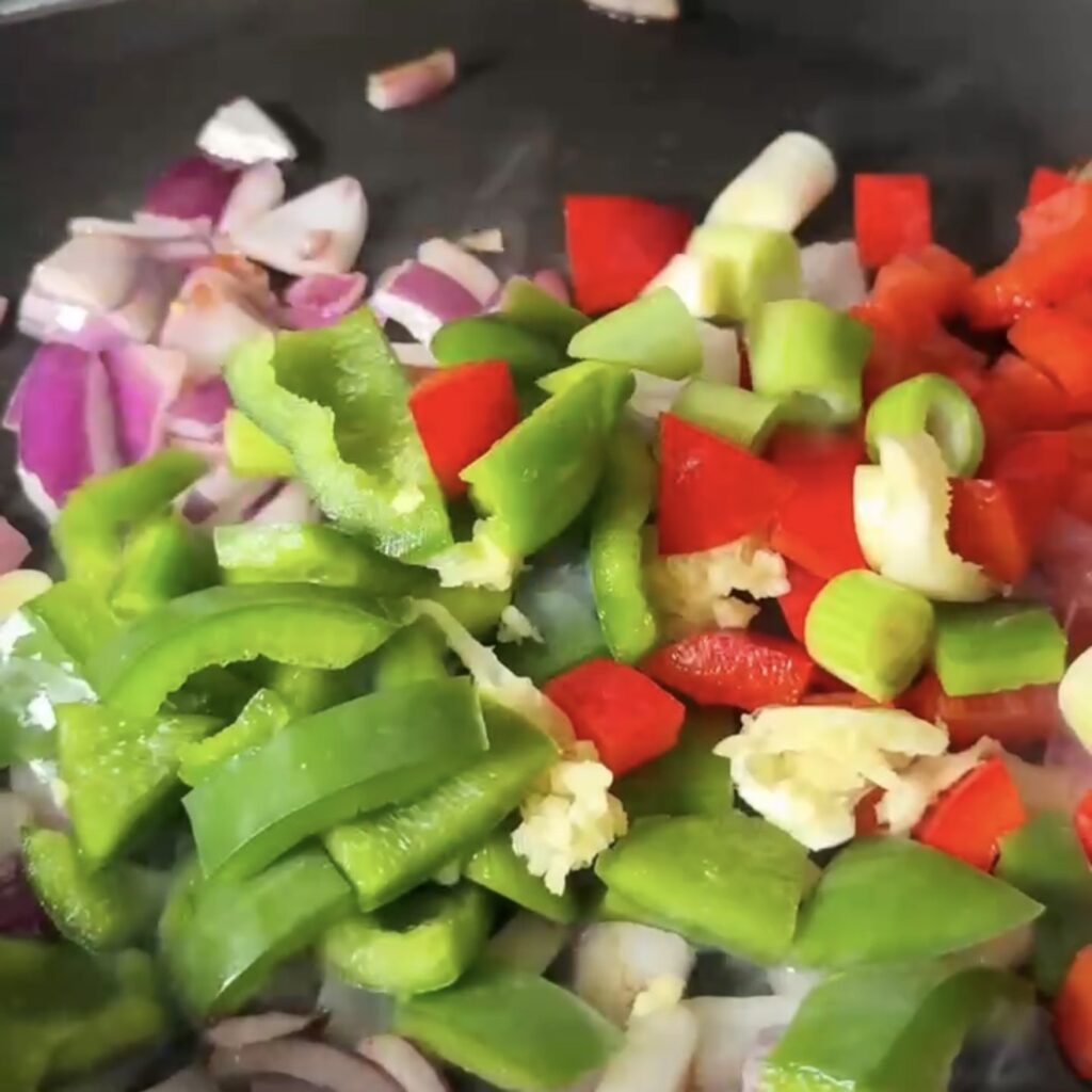 Chopped red pepper, green pepper, spring onion and red onion being added to a hot pan