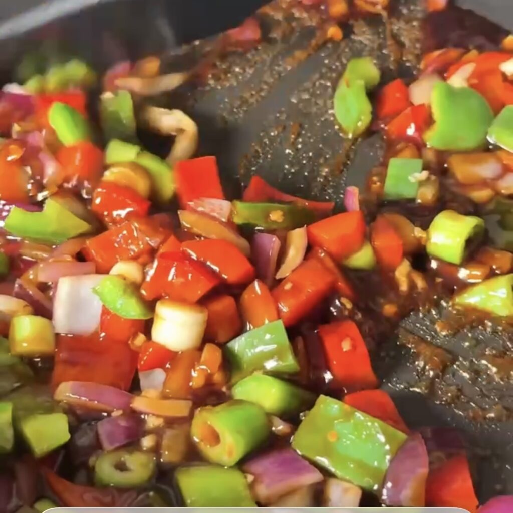 Honey garlic soy sauce being poured over the peppers and onion in the pan