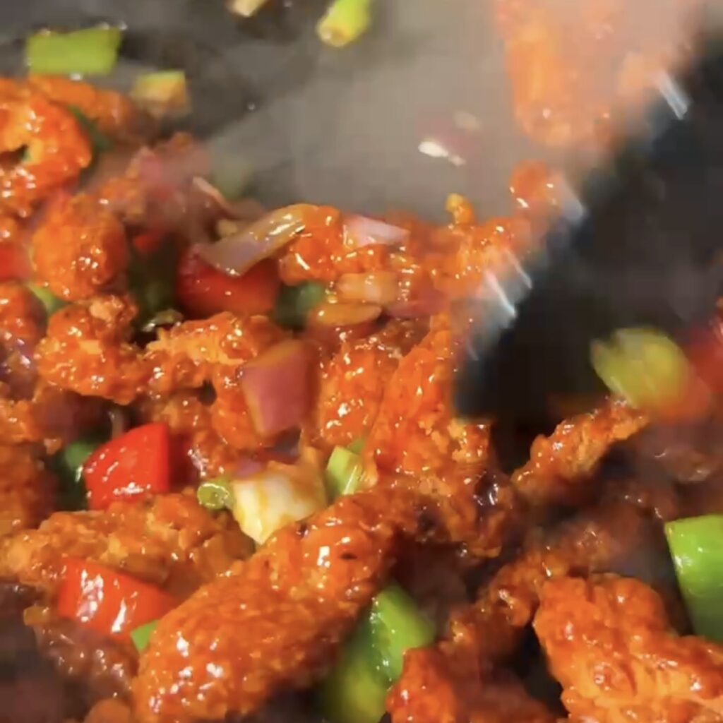 Crispy shredded chicken strips being tossed in the sticky honey garlic soy sauce with peppers and onion